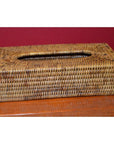 Close-up of a brown rattan tissue box on a wooden surface with a red wall in the background.