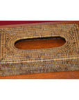 Brown hand-woven rattan rectangular tissue box with oval top opening, close-up on a wooden surface.