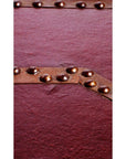 Close-up of maroon red lacquer trunk with textured finish and diagonal brass-studded metal strip.