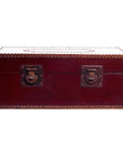 Red lacquer trunk with brown leather accents, metal studs, and two metal latches on front, close-up view.