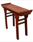Red wooden altar table with red patina finish, scroll handles, curved ends, and four straight legs, close-up view.