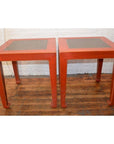 Red side tables with inset floor tiles, set on a wooden floor in front of a white brick wall.