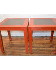 Red side tables with inset floor tiles on a wooden floor against a white wall, pair shown side by side.
