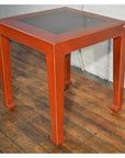 Red side tables with inset floor tiles on wood flooring next to a white brick wall, styled interior setting.