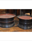 Black lacquered round offering trays with red tops on a wooden indoor floor, close-up view.