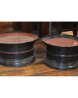Black lacquered round offering trays with red tops on a wooden indoor floor, close-up view.
