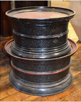 Round offering trays on a wooden floor next to a black lattice-patterned stool or drum.