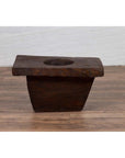 Brown wooden planter, antique Indonesian style, placed on a wood floor next to a white brick wall indoors.