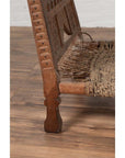 Close-up of brown wooden low chair with rope seat, rustic and weathered, on a wooden floor indoors.