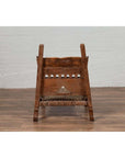 Brown wood and rope low chair with weathered finish on a wooden floor next to a white brick wall indoors.