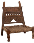 Brown wooden chair with rope seat, carved backrest, weathered finish, antique style, shown indoors.