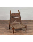 Brown wooden chair with rope seat and weathered finish on wooden floor against white wall indoors.