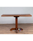 Brown wooden Indonesian console table with single plank top and pedestal base on wooden floor, front view.