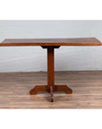 Natural wood Indonesian console table with single plank top and pedestal base on wooden floor against white brick wall.