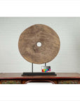 Brown wooden ox cart wheel from Thailand on black base, placed on a wooden table with white brick wall background.