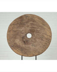 Brown wooden ox cart wheel on black base against white brick wall indoors.
