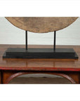 Brown wooden ox cart wheel from Thailand on black base, displayed on polished carved wooden table indoors.