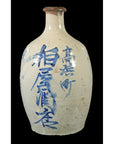 Close-up of a white ceramic sake jar with blue vertical kanji on a black background.