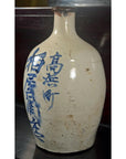 White glazed ceramic sake jar with blue calligraphy, close-up against a dark background.