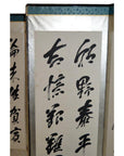 Black Chinese calligraphy on vertical scroll with silver frame, overlapping 6-panel Japanese calligraphy screen.