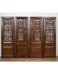 Brown carved elm screen panels with fretwork, foliage, and floral motifs leaning against a white brick wall.