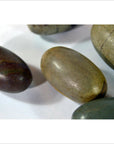 Brown and gray smooth oval Shiva Lingam fertility stones on a white surface, close-up view.