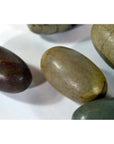 Brown and gray smooth oval Shiva Lingam fertility stones on a white surface, close-up view.