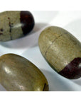 Close-up of three brown-tipped Shiva Lingam fertility stones on a white surface.