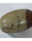 Close-up of a grey Shiva Lingam medium fertility stone with a dark brown end on a white surface.