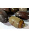 Brown and gray oval Shiva Lingam fertility stones with natural stripes, smooth texture, on white surface, close-up.