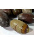 Brown and gray oval Shiva Lingam fertility stones with natural stripes, smooth texture, on white surface, close-up.