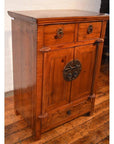 Brown wood side cabinet with metal handles, two small drawers, double doors, and lower drawer on wood floor.