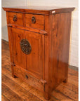Brown wooden side cabinet with two drawers, double doors, and decorative carvings on a hardwood floor.