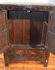 Wooden side cabinet with original decoration, open to show empty interior, placed on a wooden floor.