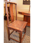 Brown wooden side chair with tall, curved backrest and square seat near a table on a carpeted floor.