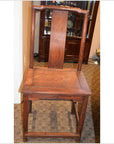 Brown wood side chair with tall curved backrest and square seat, next to a cabinet on a carpeted floor.