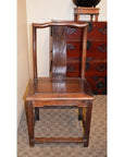 Brown wooden side chair with straight backrest and curved top on a carpet next to a wooden chest.
