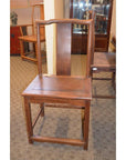 Wooden side chair with tall, straight backrest and square seat on a carpeted indoor floor.