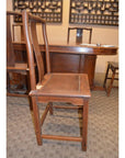 Brown wood side chair with straight backrest next to a table and other chairs in a carpeted room.