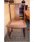 Wooden side chair with tall backrest and angular design, placed indoors near a table and cabinet.