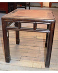 Square dark wood side table with block legs and a worn top, placed on a light wood floor.