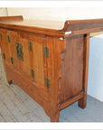 Gray wood sideboard with everted flanges and ornate metal handles, placed on a gray floor against a white wall.