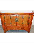 Wooden sideboard with everted flanges, ornate carvings, brass hardware, and double doors against a plain background.