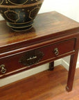 Dark wood console table with horse hoof legs and metal handles, large black bowl on wooden floor.
