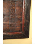 Close-up of yellow wooden signboard corner with vertical Chinese carvings, detail view.
