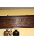 Black Chinese calligraphy signboard on yellow wall, above ceramic pottery and ornate figurine, indoor setting.