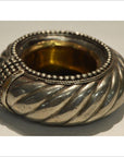 Close-up of a silver and brass dancer bracelet wine holder with twisted, beaded design on a plain surface.