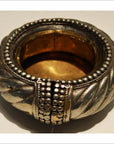 Close-up of silver and brass bracelet-style wine holder with ornate beaded and twisted patterns, gold and silver tones.
