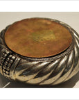 Close-up of silver and brass dancer bracelet wine holder with round, textured, twisted design and flat lid.