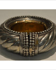 Close-up of a silver and brass twisted metal dancer bracelet wine holder with raised studs on a plain background.